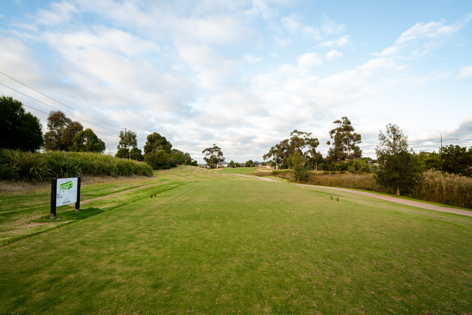 Featured is the Geelong Golf Club grass. Trees are in the background and it is a cloudy blue sky day. The golf course appears empty.